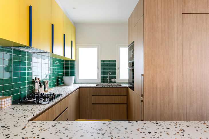 Modern kitchen featuring yellow upper cabinets, green tiled backsplash, and a speckled countertop with a gas stove.