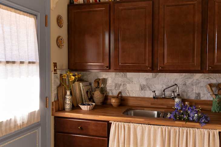 Dark wooden cabinets in newly renovated farmhouse style kitchen with sink skirt curtains.