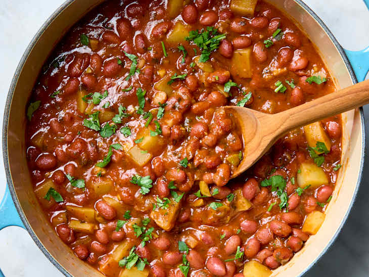 Overhead photo of Puerto Rican beans in a Dutch oven with a spoon scooping some out.