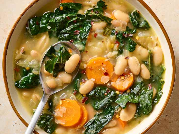 Bowl of white bean soup with kale, carrots, and spices, served with a spoon.