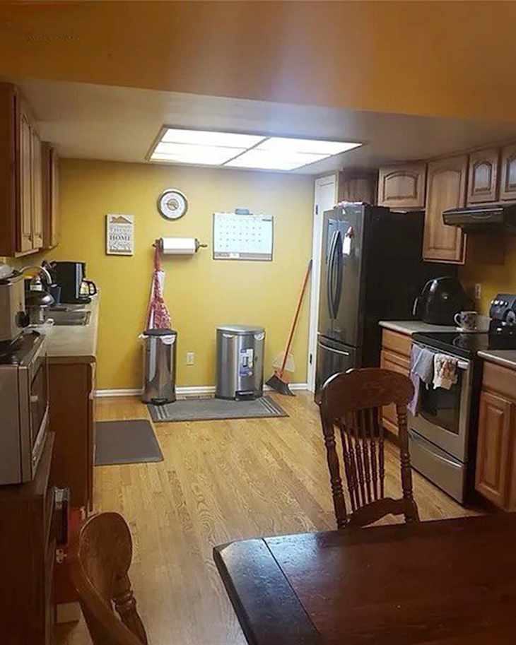 Kitchen with yellow walls, wooden cabinets, stainless steel appliances, and a wooden dining table with a chair.