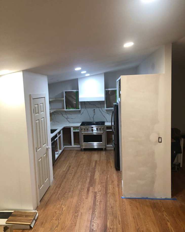 Modern kitchen with wooden flooring, stainless steel stove, and white cabinets, featuring a marble backsplash and recessed lighting.