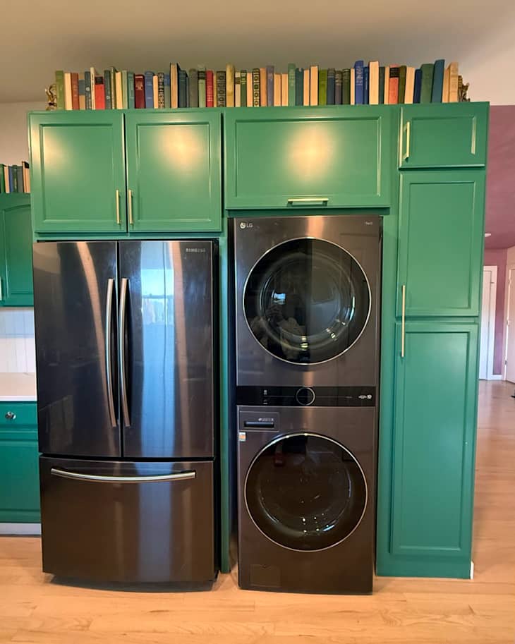 Modern kitchen featuring a green cabinet with books on top, a stainless steel refrigerator, and a stacked washer and dryer.