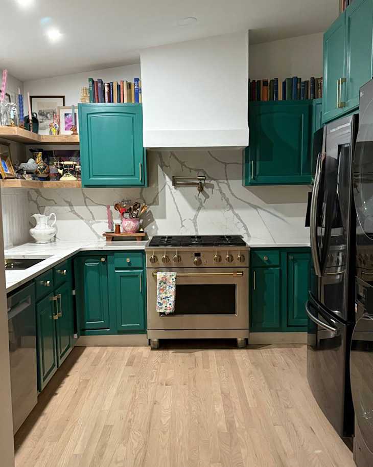 Modern kitchen featuring teal cabinets, stainless steel range, marble backsplash, and wooden flooring.