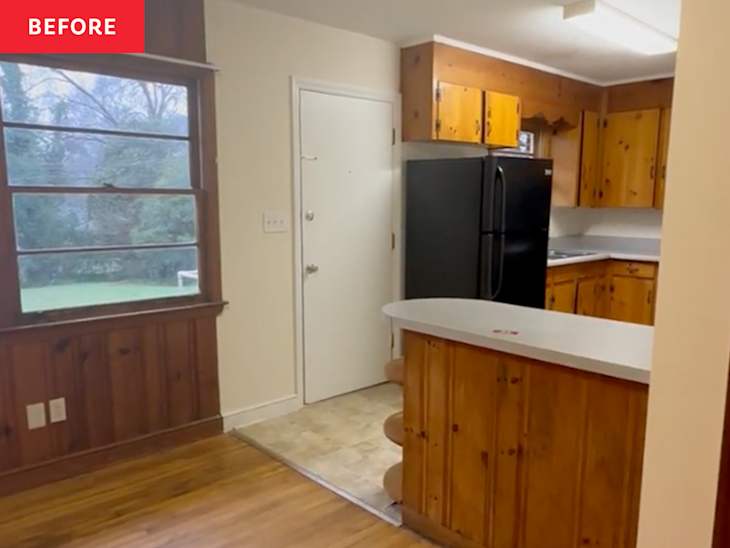 Kitchen with wooden cabinets, black refrigerator, and a small countertop bar, featuring a window view of greenery outside.