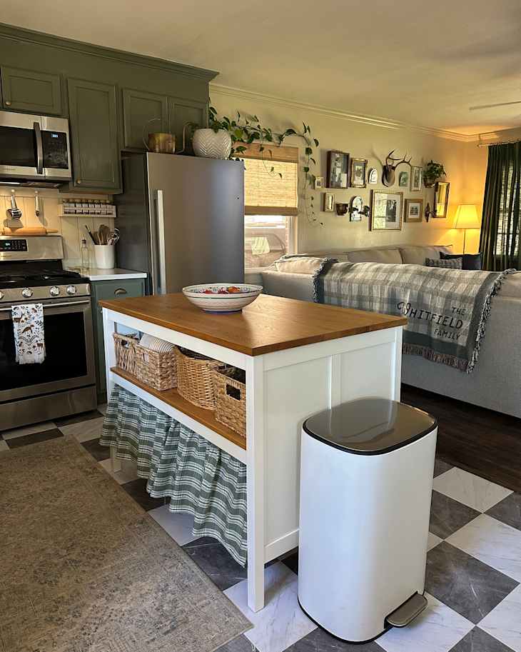 Modern kitchen with green cabinets, stainless steel appliances, a wooden island, woven baskets, and a white trash can.