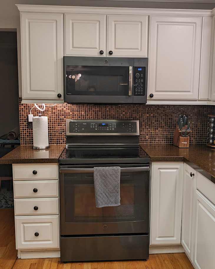 Stove top in kitchen with brown backsplash and  dark countertops before renovation.