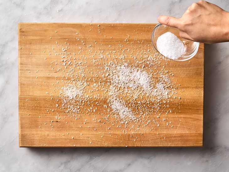 hand sprinkling coarse salt onto a wooden cutting board