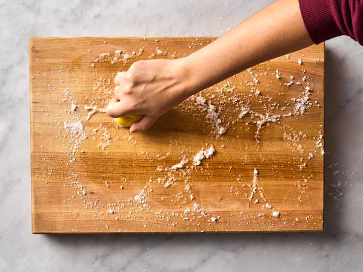 hand scrubbing lemon half on wooden cutting board