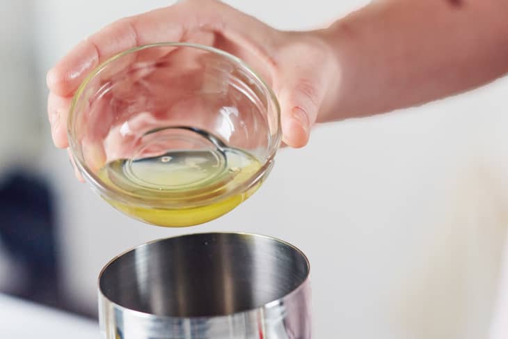 Pouring egg white from a glass bowl into a metal cocktail shaker.