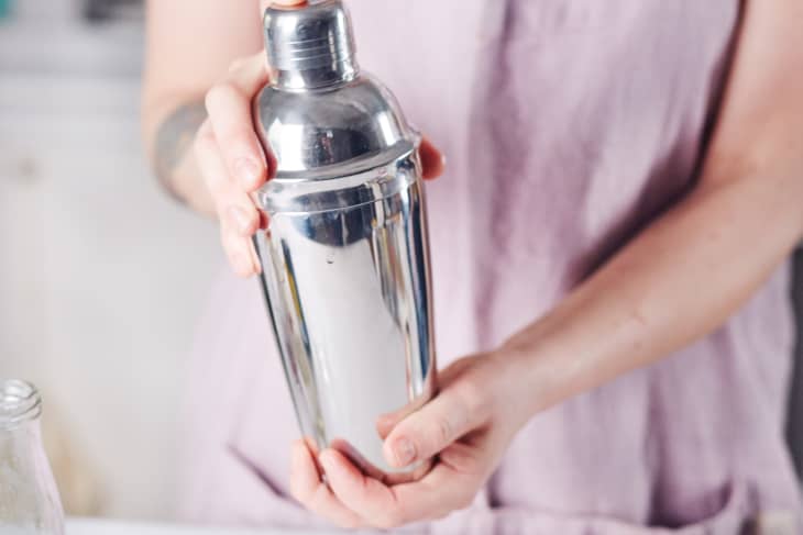 Person holding a shiny cocktail shaker, preparing a whiskey sour.