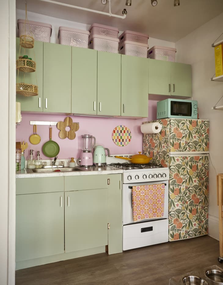 Green cabinets in pink painted kitchen with floral paper wrapped refrigerator.
