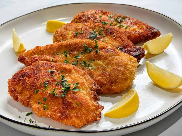 Crispy fried fish fillets garnished with parsley and served with lemon wedges on a white plate.
