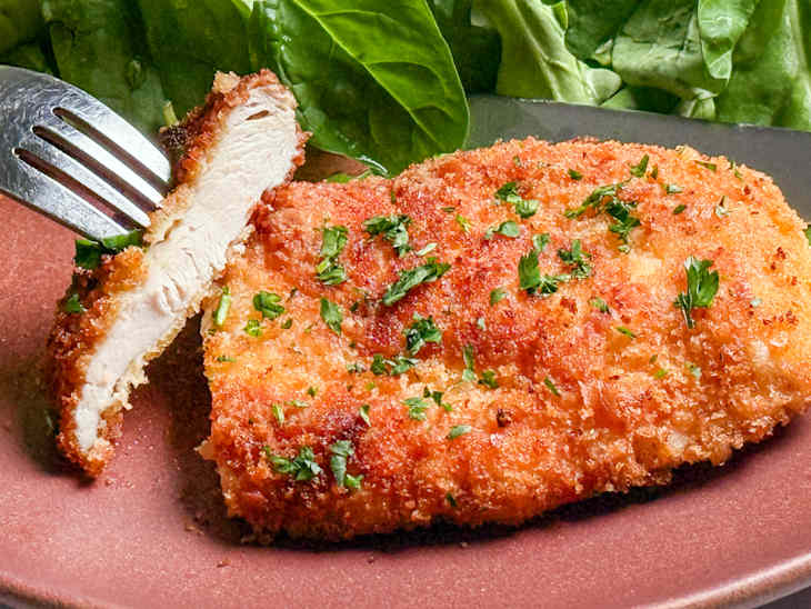 Crispy breaded chicken cutlet garnished with parsley, served on a plate with fresh spinach.