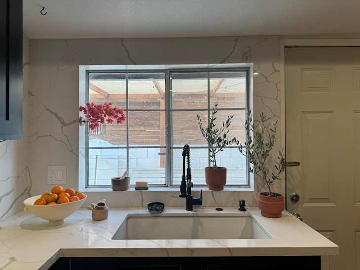 Toilet paper holder mounted on inside of kitchen window filled with decorative flowers.