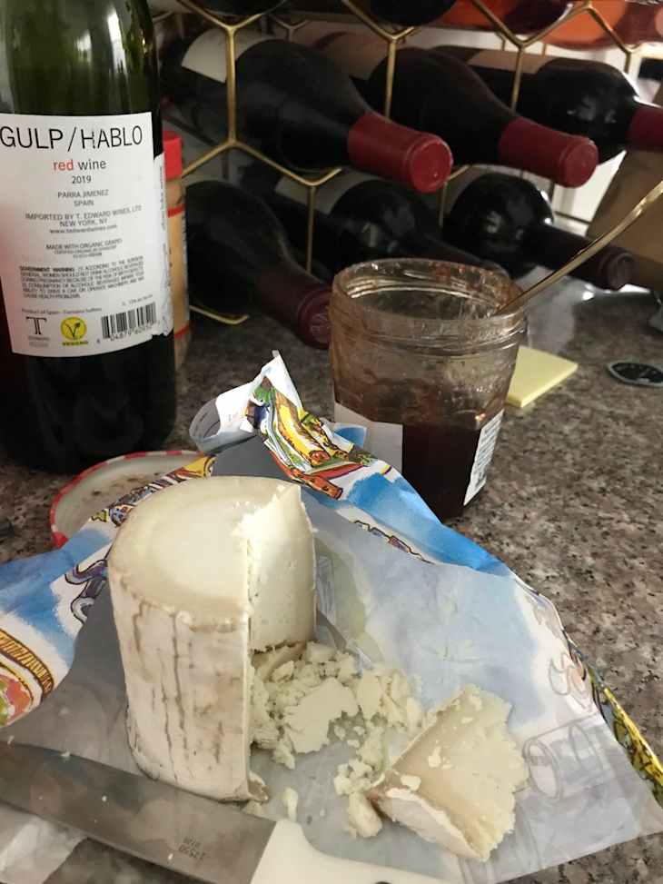 unwrapped cheese on a countertop with open jar of preserves