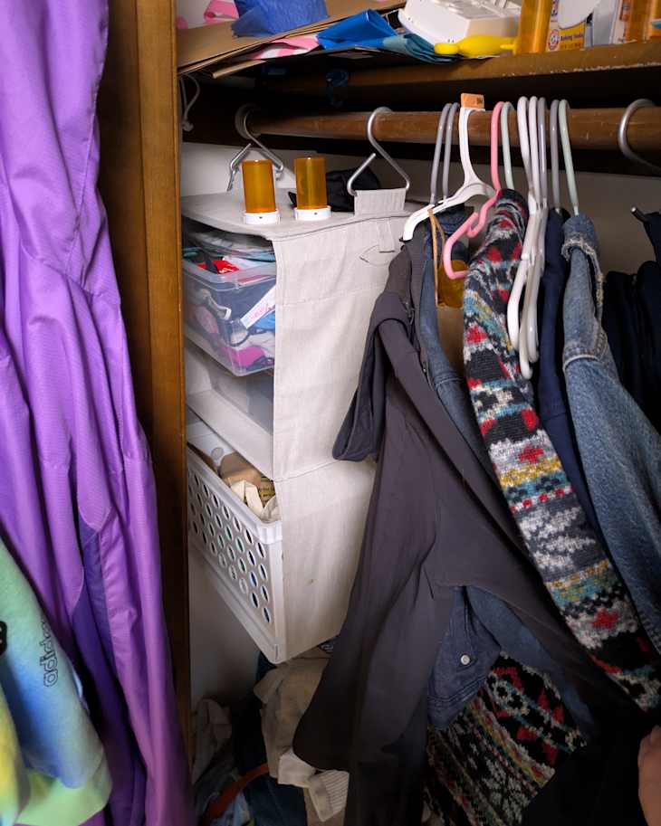 Closet interior with hanging clothes, a fabric storage bin, and a white basket filled with items.
