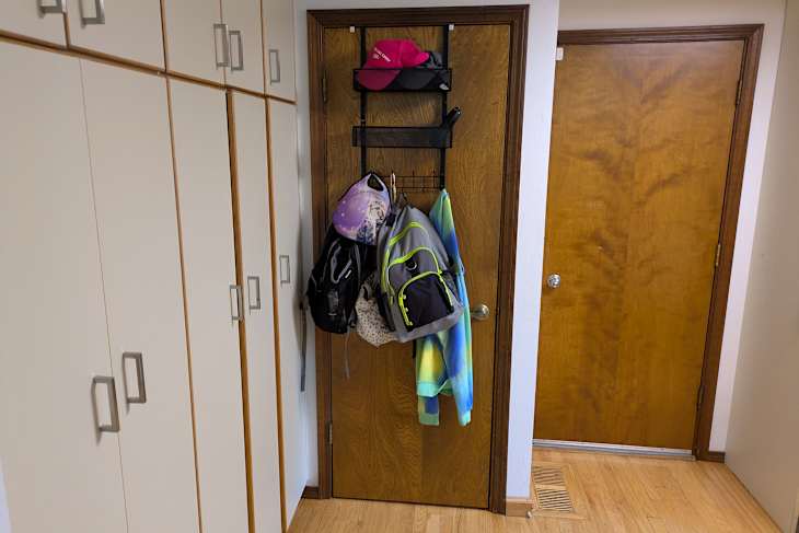 Entryway with storage cabinets, a door, and a rack holding backpacks, a hoodie, and a cap.