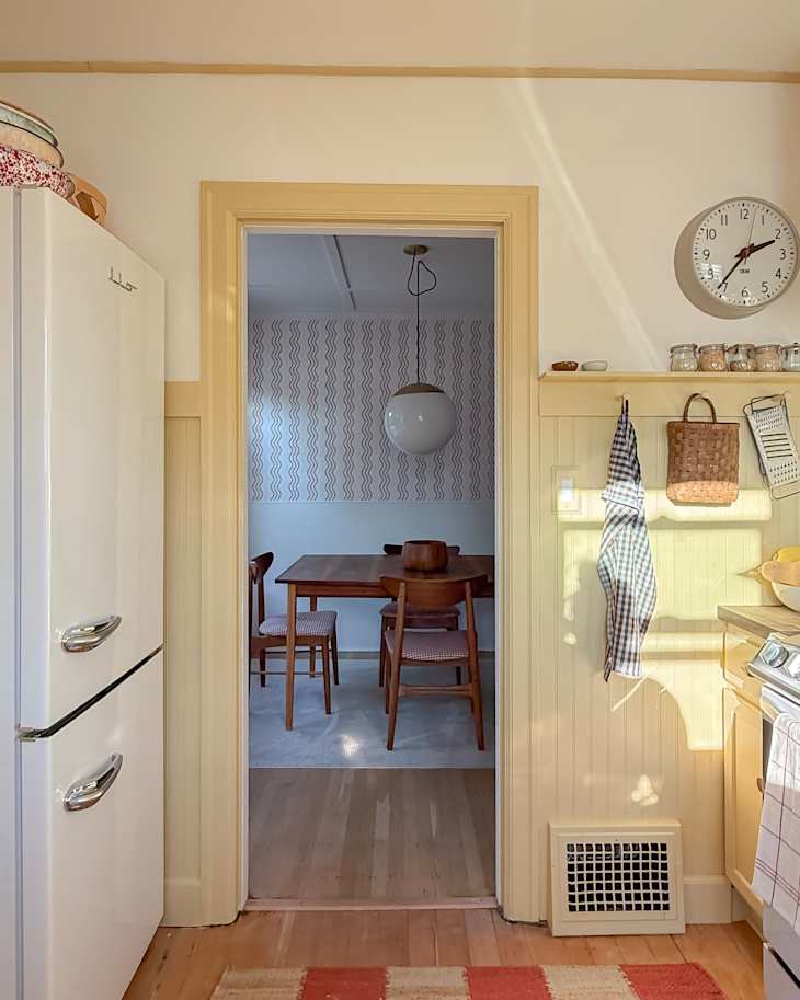 View from a kitchen into a dining area featuring a wooden table, four chairs, and a patterned wall.
