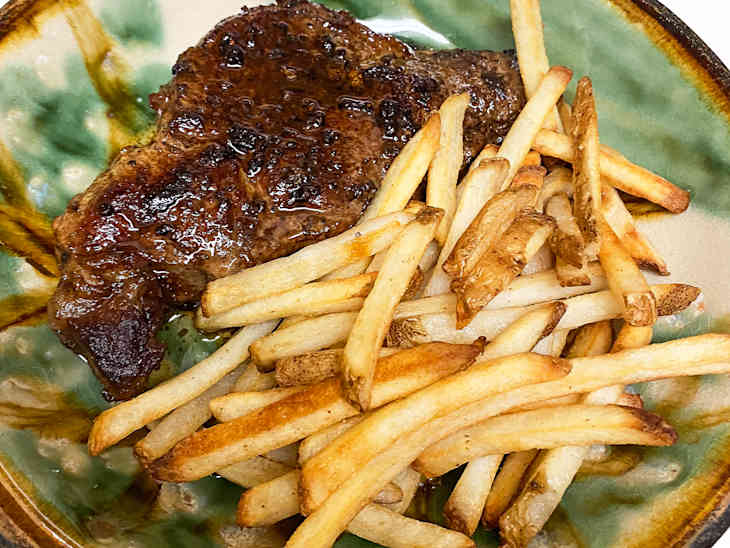 Juicy grilled steak served with crispy golden French fries on a decorative plate.