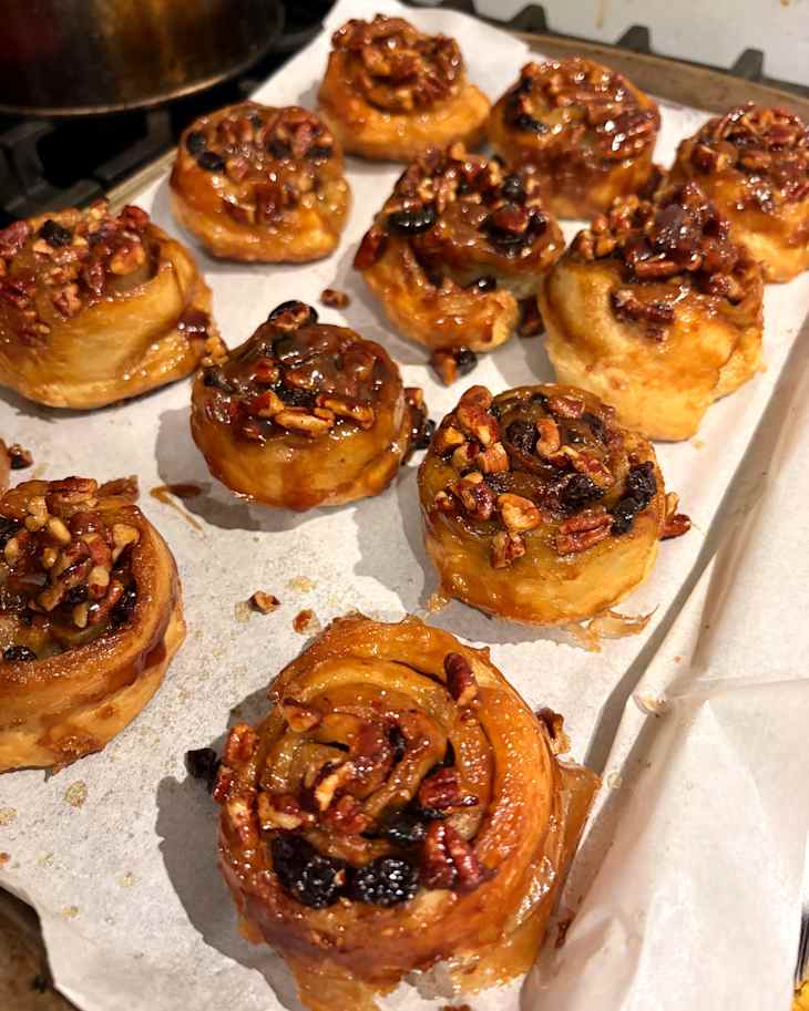 Caramelized cinnamon rolls topped with pecans and raisins on parchment paper, freshly baked and golden brown.