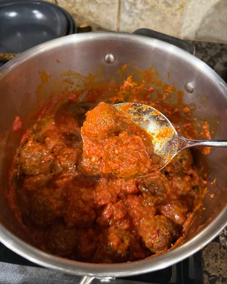 Tomato sauce covered meatballs cooked in pan.
