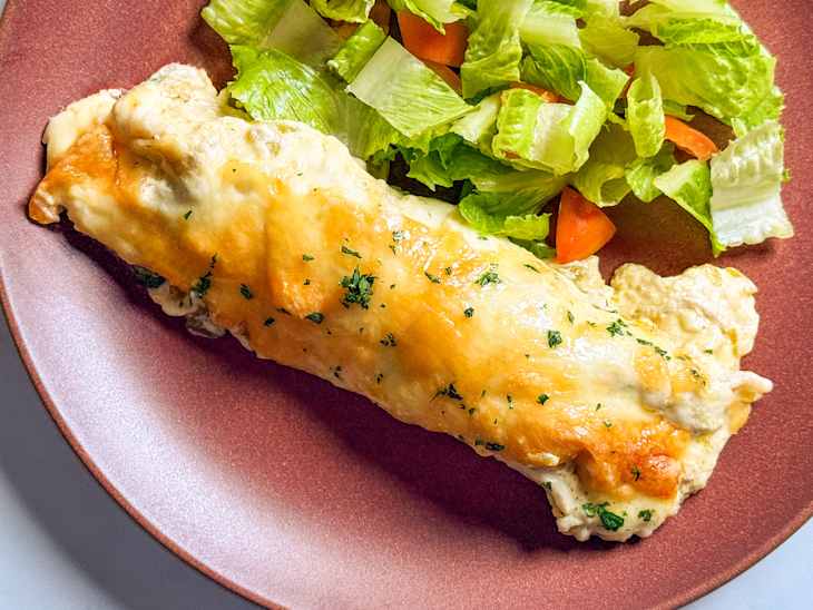 Chicken enchilada on plate with side salad.
