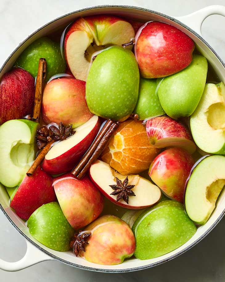 A pot filled with red and green apple slices, cinnamon sticks, and star anise, submerged in water.