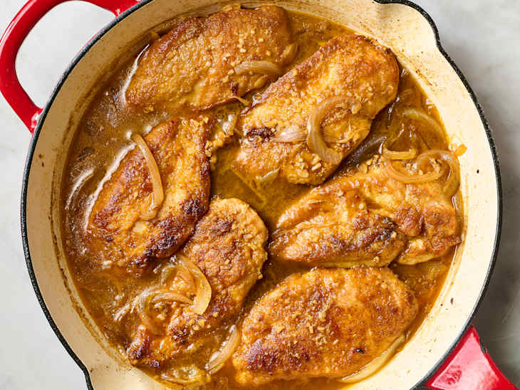 Pan-seared chicken breasts in a rich brown sauce with onions and herbs in a red Dutch oven.