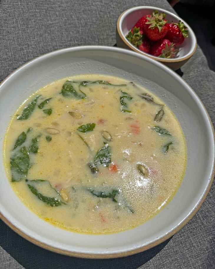 Bowl of creamy chicken soup next to a bowl of strawberries