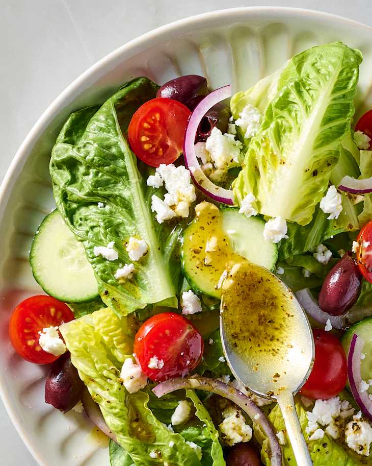 Fresh salad with romaine lettuce, cherry tomatoes, cucumbers, red onion, olives, and feta cheese, drizzled with dressing.