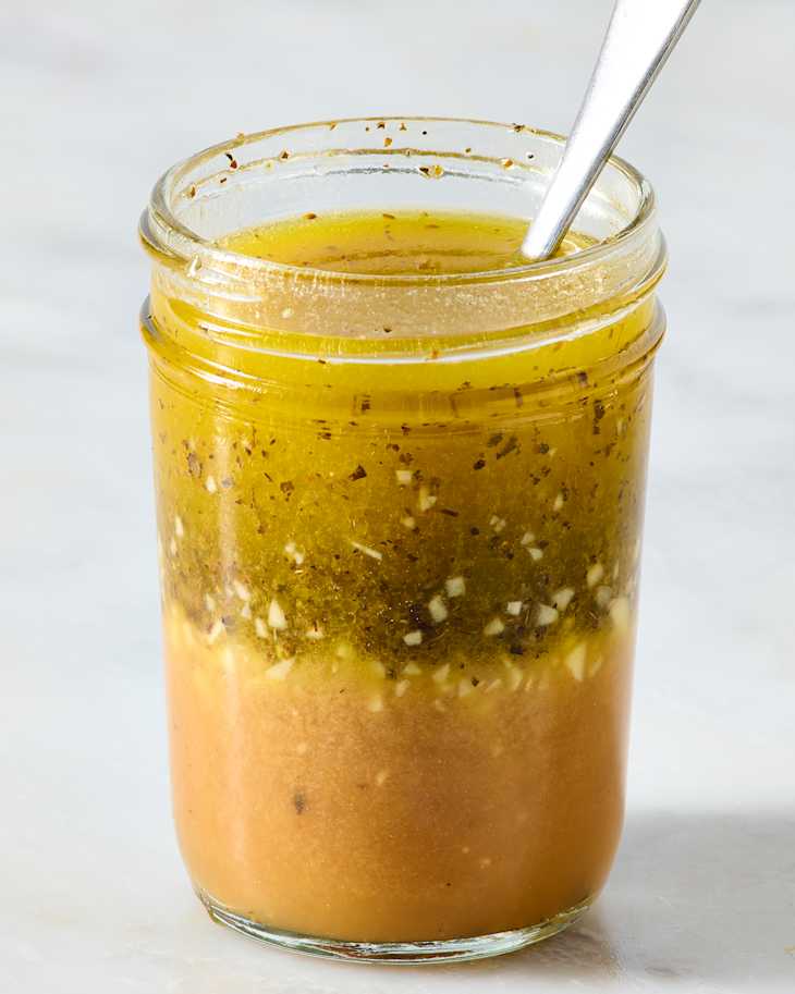 A glass jar filled with layered salad dressing, featuring a golden top layer with herbs and a creamy bottom layer.