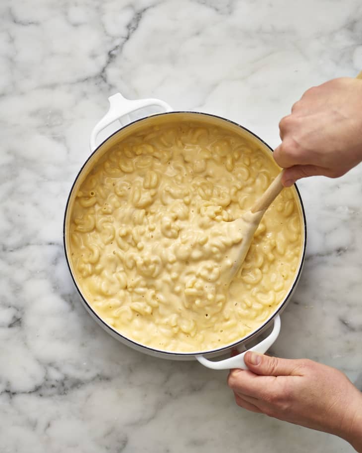 Creamy macaroni and cheese in a pot, being stirred with a wooden spoon.
