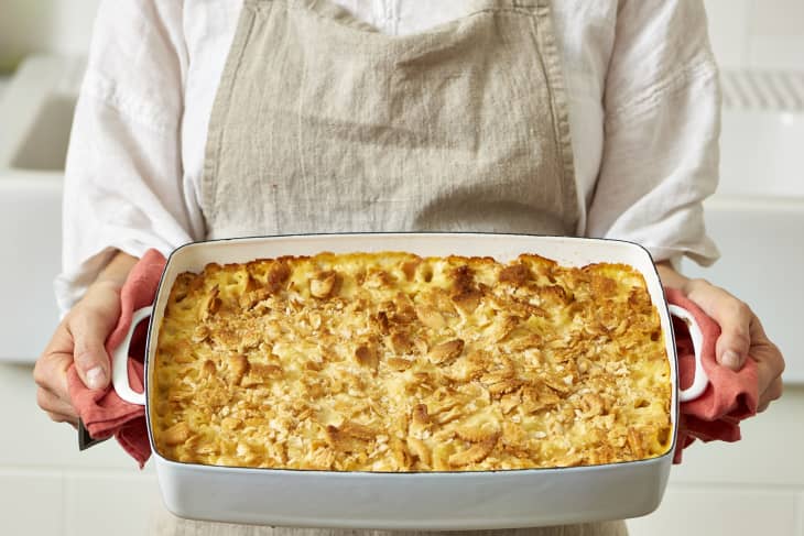 Creamy mac and cheese casserole topped with golden breadcrumbs in a baking dish held by a person.