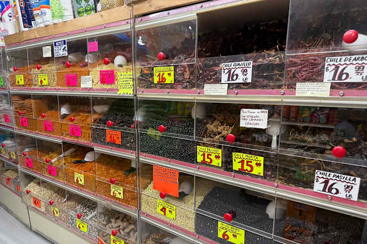 A variety of dried spices and legumes in clear bins.