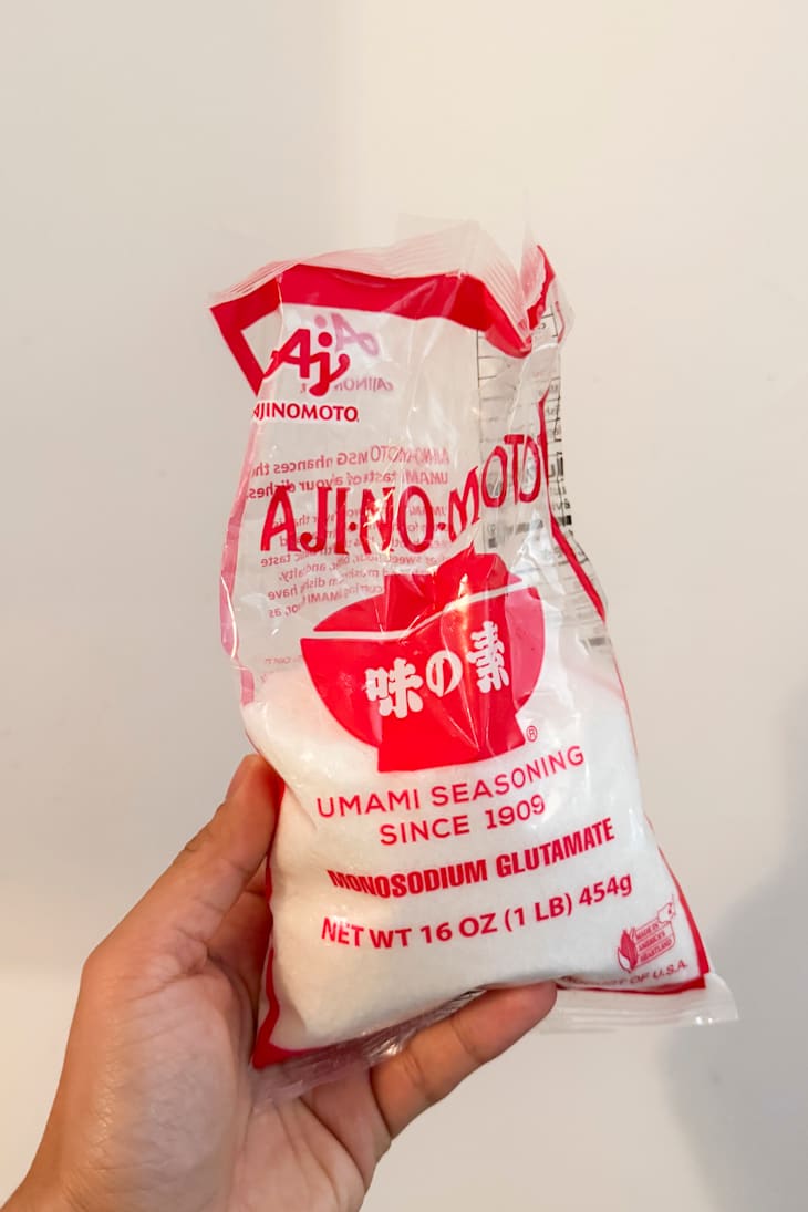 A hand holding a bag of Ajinomoto umami seasoning.