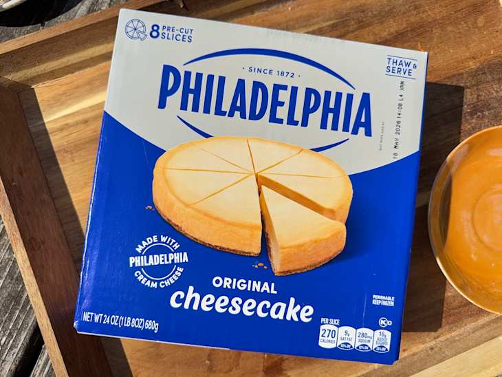 Box of Philadelphia Original Cheesecake with pre-cut slices, placed on a wooden surface next to a small orange dish.