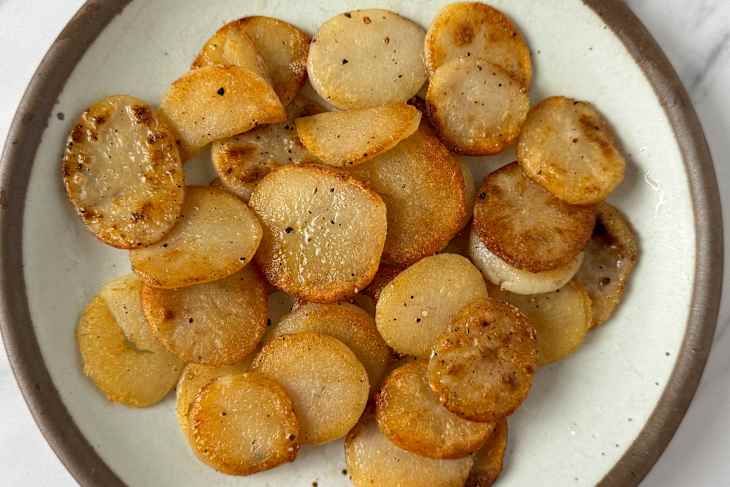 Crispy, golden-brown sliced potatoes arranged on a round plate with a brown rim.