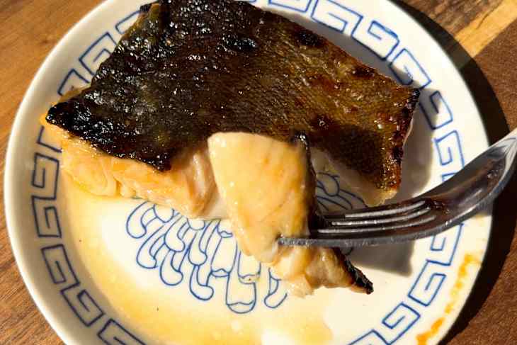A piece of cooked fish with crispy skin on a decorative plate.