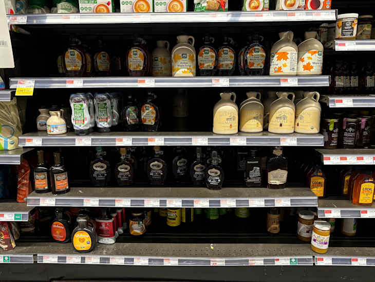 Shelves stocked with various brands of maple syrup, honey, and sweeteners in different containers.