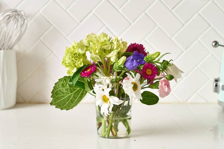 Vibrant bouquet with daisies, hydrangeas, and purple flowers in a glass vase on a kitchen counter.