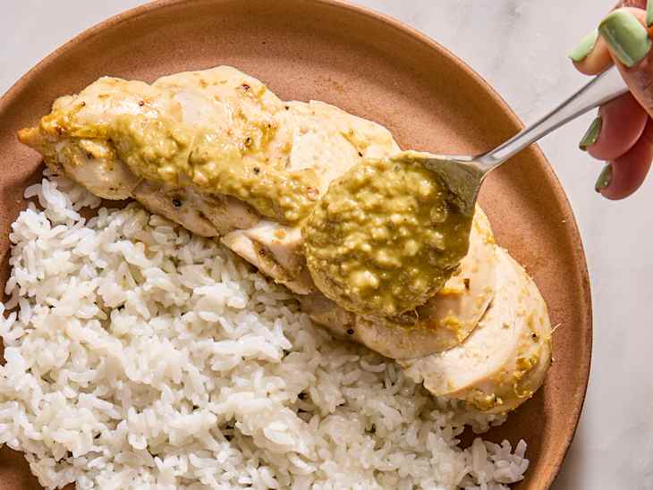 Sliced chicken breast topped with green sauce, served with fluffy white rice on a brown plate.