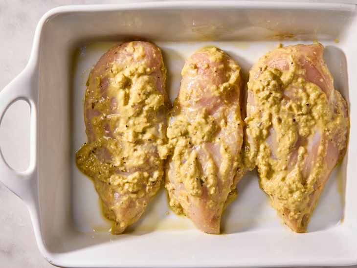 Three chicken breasts coated in a creamy marinade of lime leaf sambal sauce, placed in a white baking dish.
