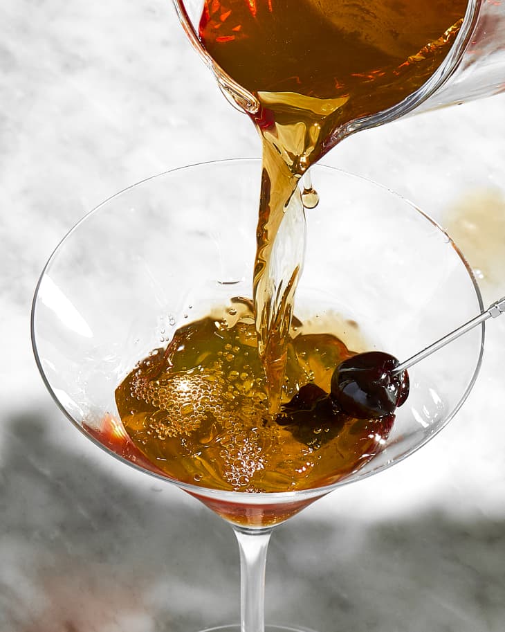 overhead shot of a manhattan being poured into a martini glass.