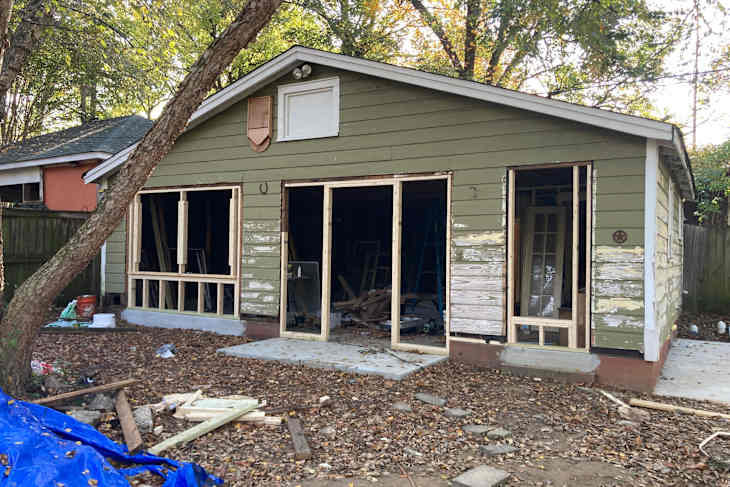 Renovation of a green house with open door frames, surrounded by fallen leaves and construction materials.