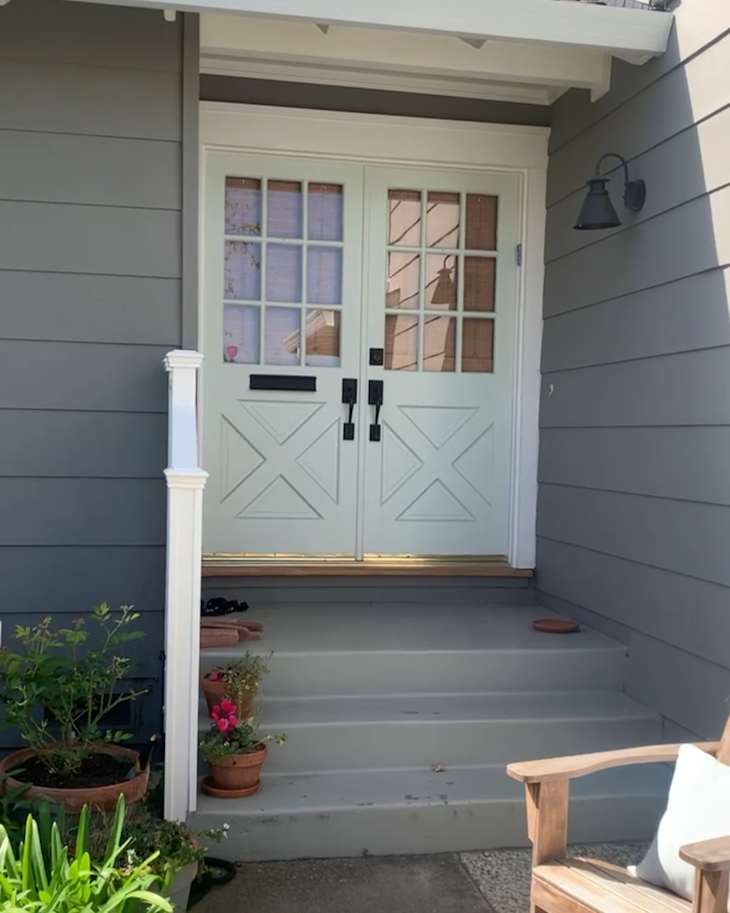 Front entrance with double light green doors, potted plants, and a wooden chair on the porch.