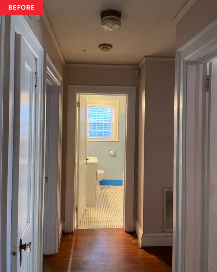 Door open in showing bathroom at the end of a long hallway before renovation.