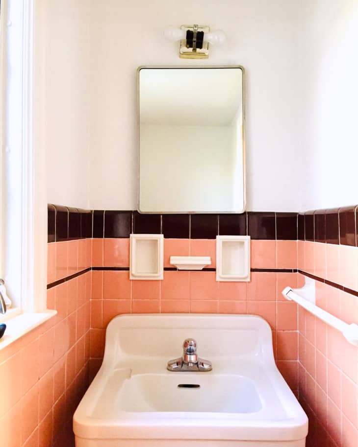 Pink tile with black tile border hangs on white bathroom with white sink and toilet.
