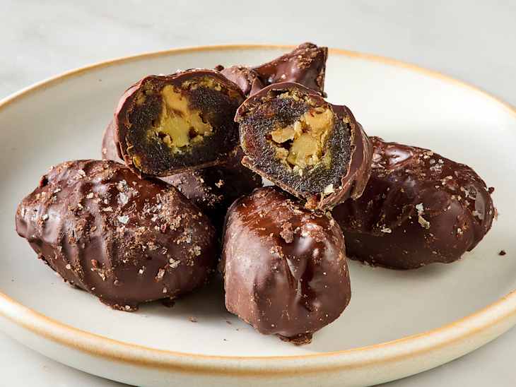 Chocolate-covered treats with a nut filling, some cut in half to reveal the interior, on a plate.
