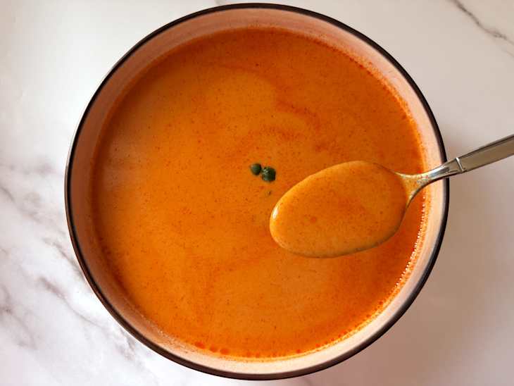 Creamy orange soup in a bowl with a spoon, garnished with small green herbs.